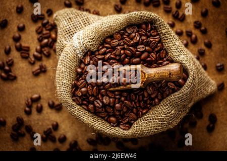 Roasted coffee beans in burlap sack. Sackcloth bag with grains on grunge textured background. Coffee export, Top view selective focus, shallow depth o Stock Photo