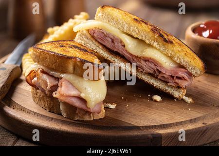 Closeup of grilled ham and cheese sandwich cut in half with french fries on a wooden platter Stock Photo