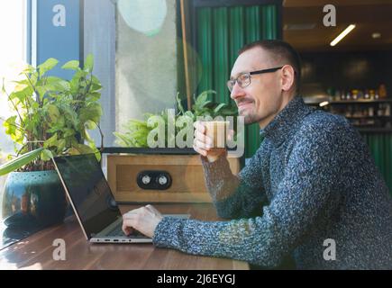 Satisfied businessman sitting near computer, holding coffee mug and thinking about his success. Stock Photo