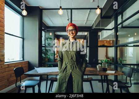 Happy female entrepreneur smiling at the camera while standing in an office boardroom. Cheerful Muslim businesswoman wearing a headscarf in a modern w Stock Photo