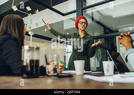 Creative businesswoman having a meeting with her team in a boardroom. Muslim businesswoman using sticky notes while discussing her ideas. businesswoma Stock Photo