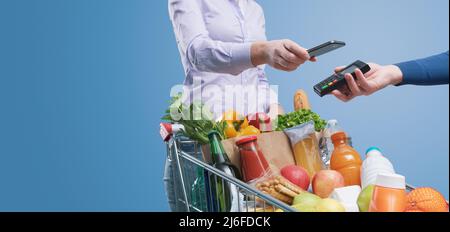 Woman paying for groceries using her smartphone, NFC payments concept Stock Photo