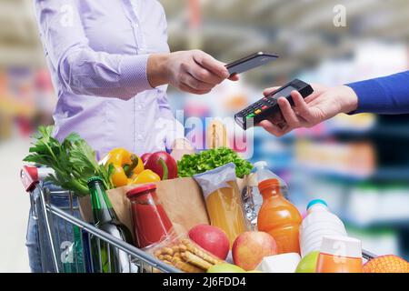 Woman paying for groceries using her smartphone, NFC payments concept Stock Photo