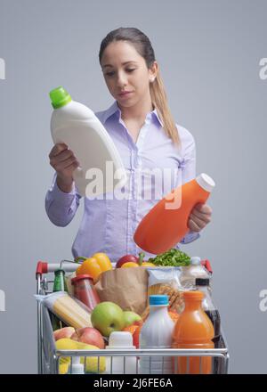 Woman doing grocery shopping at the supermarket and comparing products, she is checking two bottles of laundry detergent Stock Photo