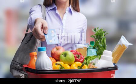 Woman holding a full shopping basket and paying for groceries using a credit card Stock Photo