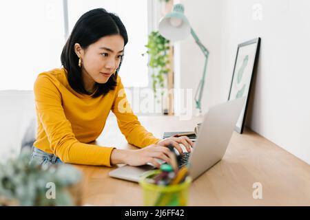Young asian woman using a laptop computer while studying online from home. Stock Photo