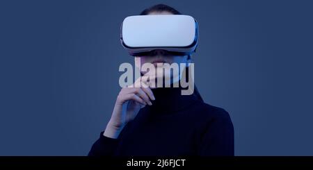 Young beautiful woman wearing a VR headset and experiencing virtual reality, futuristic technology concept Stock Photo