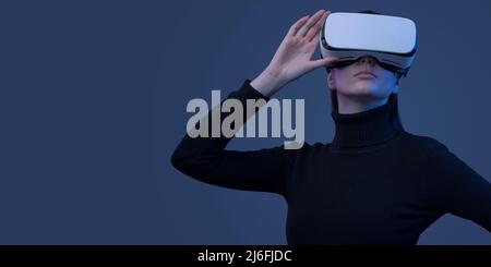 Young beautiful woman wearing a VR headset and experiencing virtual reality, futuristic technology concept Stock Photo