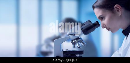 Young researcher working in the lab, she is looking through a microscope and checking samples, medical research concept Stock Photo