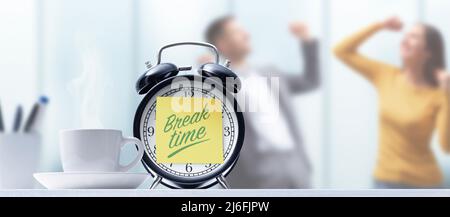 Business people taking a break in the office, alarm clock with sticky note in the foreground Stock Photo