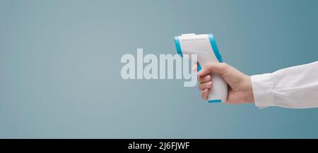 Doctor holding an infrared thermometer and measuring temperature, coronavirus prevention concept Stock Photo