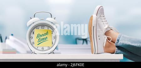 Woman relaxing with feet up in the office and alarm clock with sticky note, it's break time Stock Photo