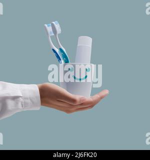 Dentist showing toothbrushes and toothpaste in a cute smiling toothbrush holder, dental hygiene concept Stock Photo