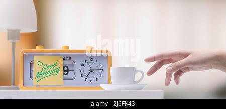 Alarm clock with good morning message and coffee cup on the bedside table Stock Photo