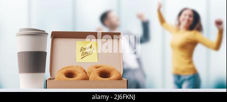 Happy business people taking a break during work hours, coffee and donuts in the foreground Stock Photo