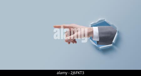 Businessman hand pointing and coming out of a hole in paper Stock Photo