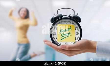 Hand showing a vintage clock with sticky note and happy woman jumping and celebrating, it's break time Stock Photo