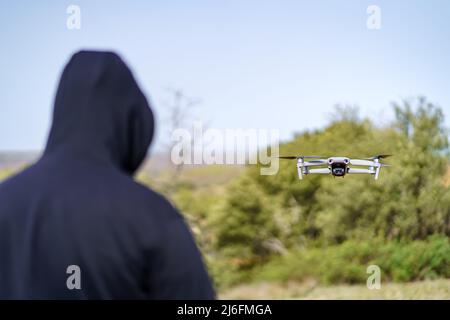 Man flying a drone in front of him in the field with trees. Stock Photo