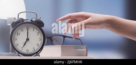 Woman turning off a vintage alarm clock, she wakes up early Stock Photo