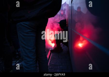 01 May 2022, Hessen, Frankfurt/Main: A participant sits in the wheel well of a bus while pyrotechnics were ignited next to him. In the evening, an alliance of several left-wing organizations demonstrated in Frankfurt am Main. Photo: Hannes P. Albert/dpa Stock Photo