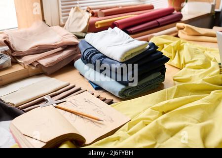 Group of objects on workplace of contemporary tailor or fashion designer including stack of folded textile and lookbook or notebook with sketches Stock Photo