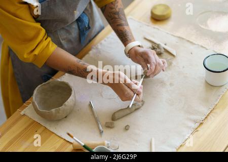 Woman ceramist make pottery cup in studio. Creative girl pottery master with tattoo shaping pot mug Stock Photo