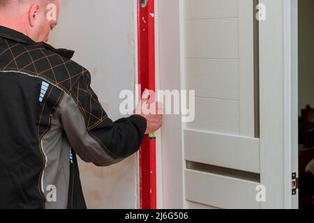 Repair work of home on hands using red level measuring surface of new white wooden door Stock Photo