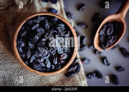 black raisins in wooden bowl with black background
