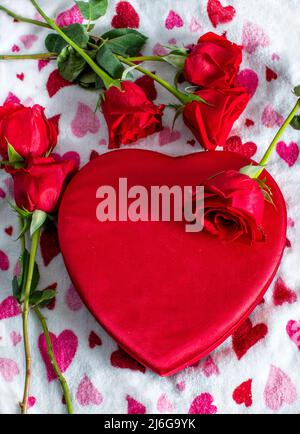 A red heart box of chocolates has red roses all over and a cute back ground of red and pink hearts Stock Photo