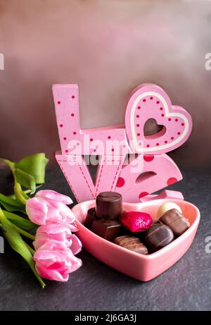 pink love cut out with pink tulips, and a pink candy heart filled with fancy chocolates Stock Photo