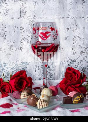 romantic roses, wine and chocolates are in a still life with lace curtain background Stock Photo