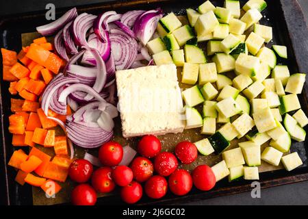 Raw Vegetables and a Block of Feta Cheese on a Sheet Pan: Chopped vegetables, cherry tomatoes, and a block of feta on a parchment-lined sheet pan