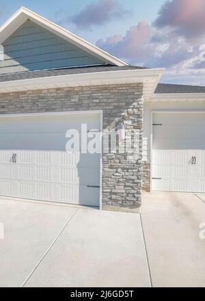 Vertical Puffy clouds at sunset Three-car side hinged garage doors with stone veneer wall siding Stock Photo