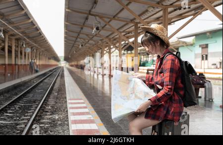 Young woman traveler with backpack looking to map while waiting for train, Asian backpacker on railway platform at train station. Holiday, journey Stock Photo