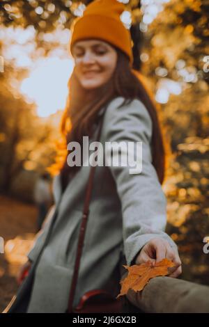 A young girl is standing outside alone on the street with sunny rays and holding a maple leaf in her hand Stock Photo