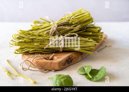 Raw pasta fettuccine made with spinaches on cutting board with concrete background Stock Photo