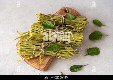 Bundles of raw pasta fettuccine with spinaches on wooden cutting board and concrete background Stock Photo