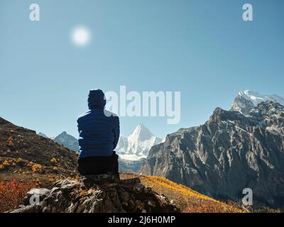 rear view of asian woman sitting on top of a nearby mountain looking at Mount Yangmaiyong (or Jampayang in Tibetan) in Yading, Daocheng County, Sichua Stock Photo