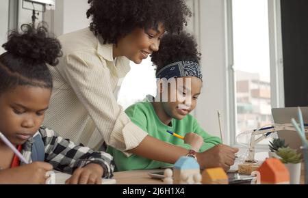 African American female teacher standing with pupils teaching writing lesson in modern classroom. Stock Photo