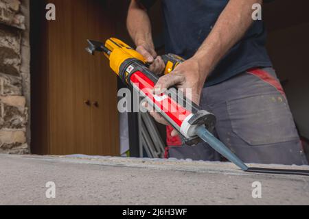 Modern window instalation in an old house. Worker applying sealant or silicone seal onto window shelf or ledge to make a good seal with the new window Stock Photo