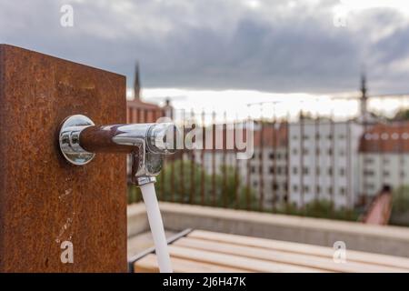 Water fountain made of chrome installed in a rusty wall in the city of Steyr, Upper Austria. Stock Photo
