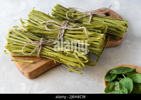 Bundles of raw pasta fettuccine with spinaches on wooden cutting board and concrete background Stock Photo