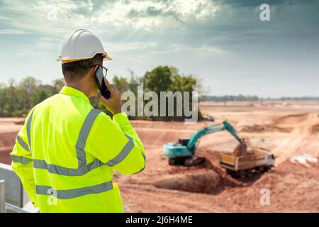 A civil engineer is using a construction telephone on the construction site in the background with loaders and dumpers. Stock Photo