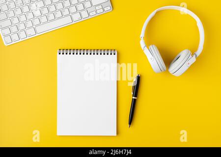 Workspace surface. Notebook, pen, headphones and portable keyboard on yellow background, flat lay Stock Photo