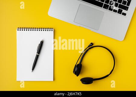 Contemporary workspace on yellow background. Notebook with pen, laptop and digital headset Stock Photo