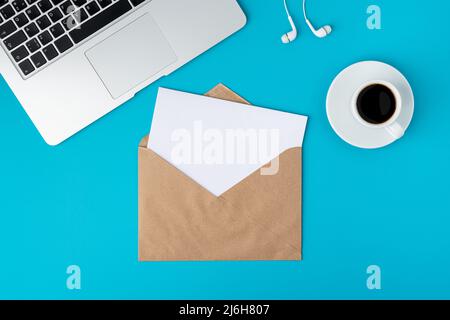 Open envelope with blank paper sheet on turquoise background. Keyboard, cup of coffee and earphones Stock Photo