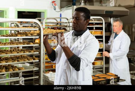 African baker arranging trays with bakery products on trolley Stock Photo