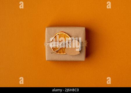 Craft gift package on orange background. Handcrafted cardboard box in wrapping paper and adornment. Stock Photo