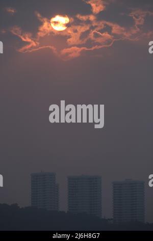 Sun shines through heavy clouds above hill with residential buildings Stock Photo