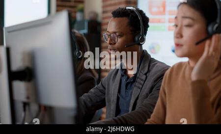 Male call center operator using headset to help people, giving telemarketing assistance to clients on helpline. Person working at customer support service office, offering advice. Stock Photo